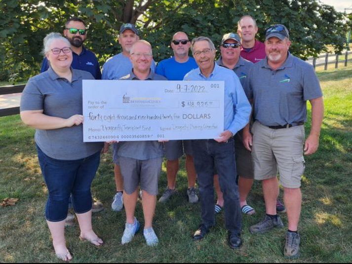 Photo of golf committee members presenting oversized check with tree in background